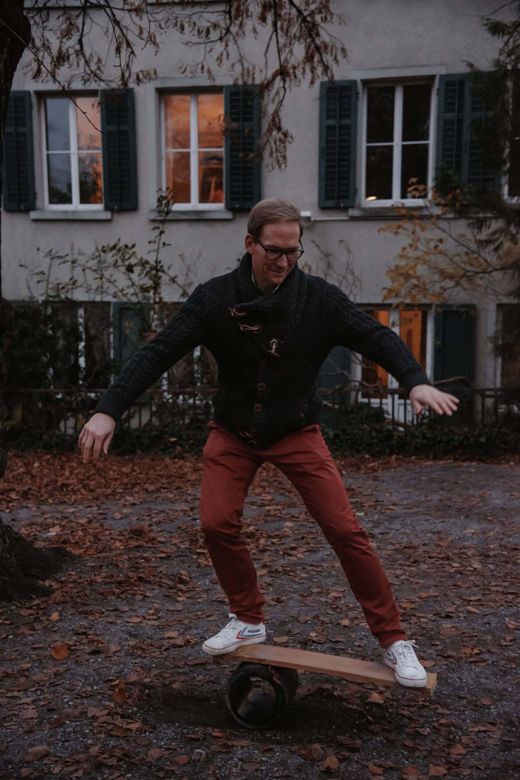 Mann balanciert auf einem Holzbrett über einer Rolle in einem herbstlichen Hof