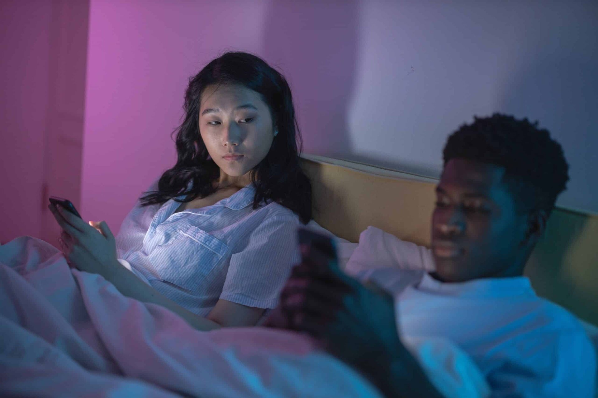 Paar liegt abends im Bett, beide schauen auf ihr eigenes Handy statt zueinander