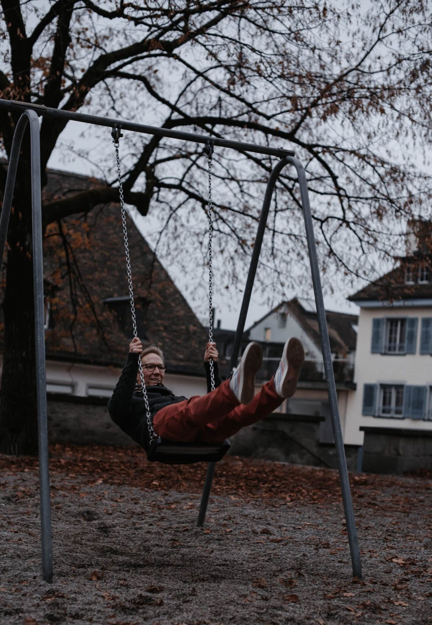 Erwachsener Mann schwingt auf einer Schaukel auf einem Spielplatz im Herbst